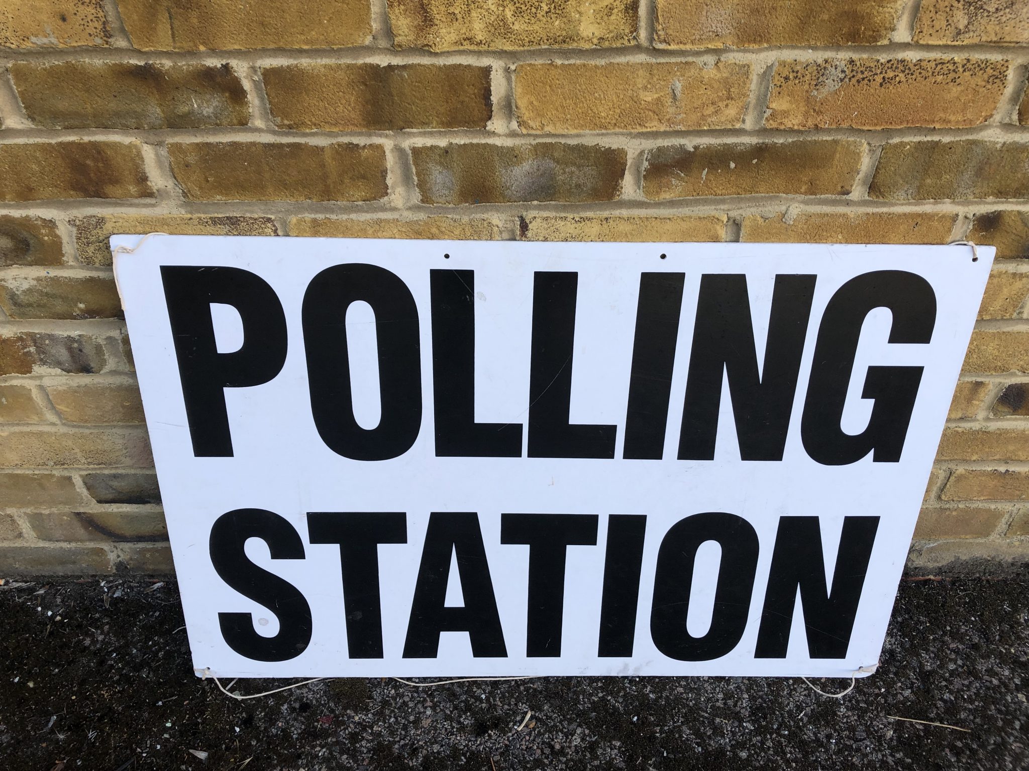 Polling Station - sign written in block caps on white, leaning against a brick wall