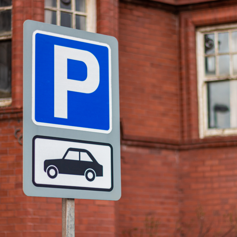 Parking sign, capital P in white on a bright blue background, with an illustration of a car underneath in black on a white background