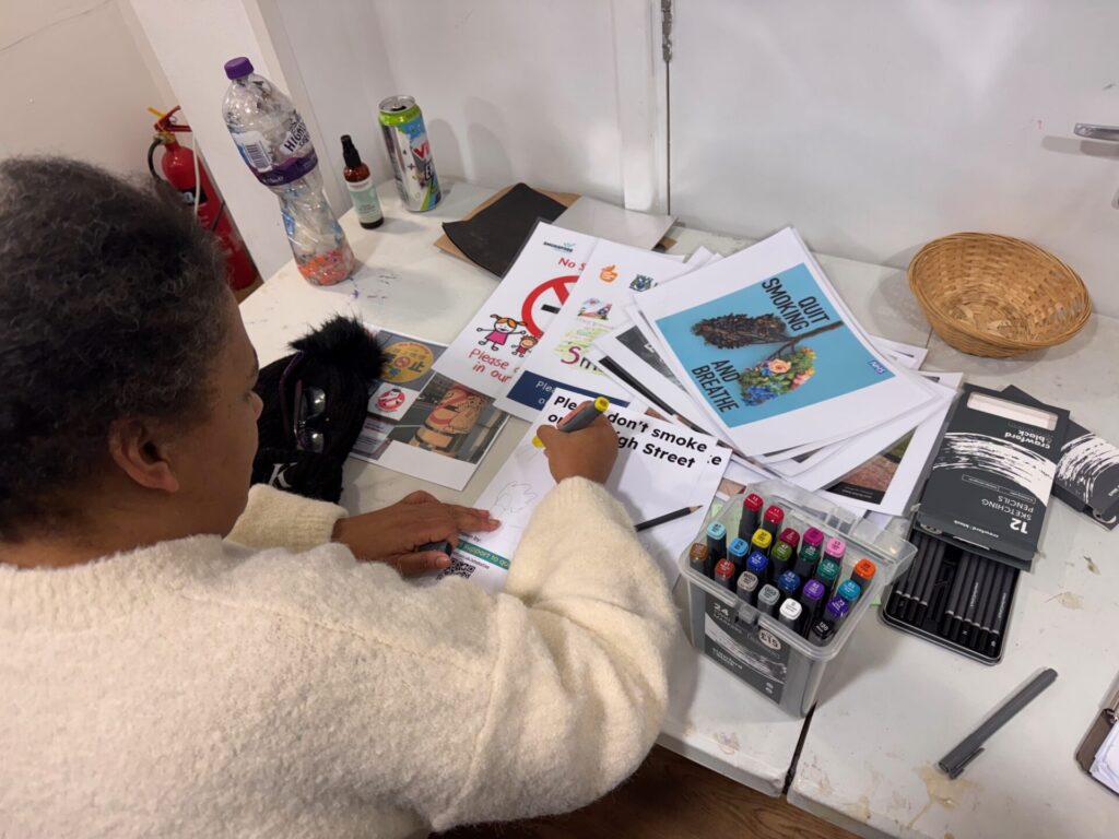 Photo shows a woman sitting at a desk and she is designing a poster.