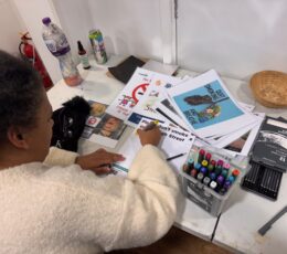 Photo shows a woman sitting at a desk and she is designing a poster.